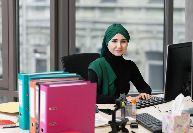 muslim businesswoman in hijab working at desk with computer and colorful folders in office.png
