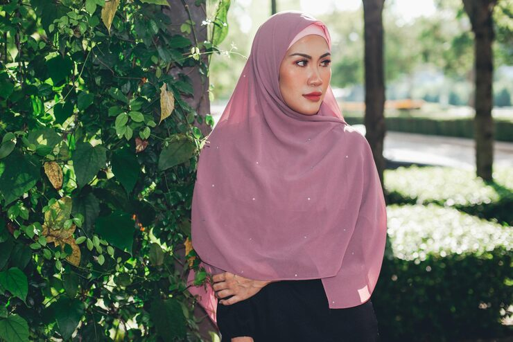 woman in pink hijab standing by green foliage in park.png
